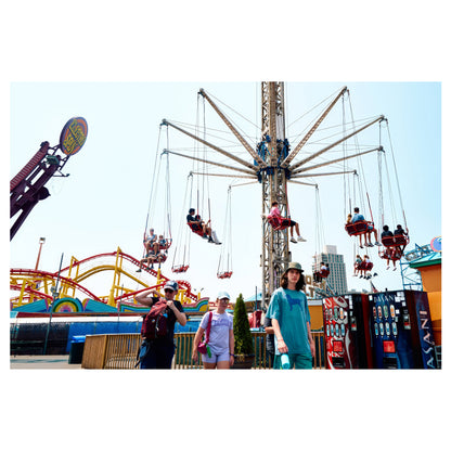 The Wave Swinger swing-carousel ride turning above the Coney Island amusement park, riders lifted into the air over the fairground. A color fine-art photograph by Chloe Albert from the Coney Island series, printed on Hahnemühle Photo Rag Bright White.