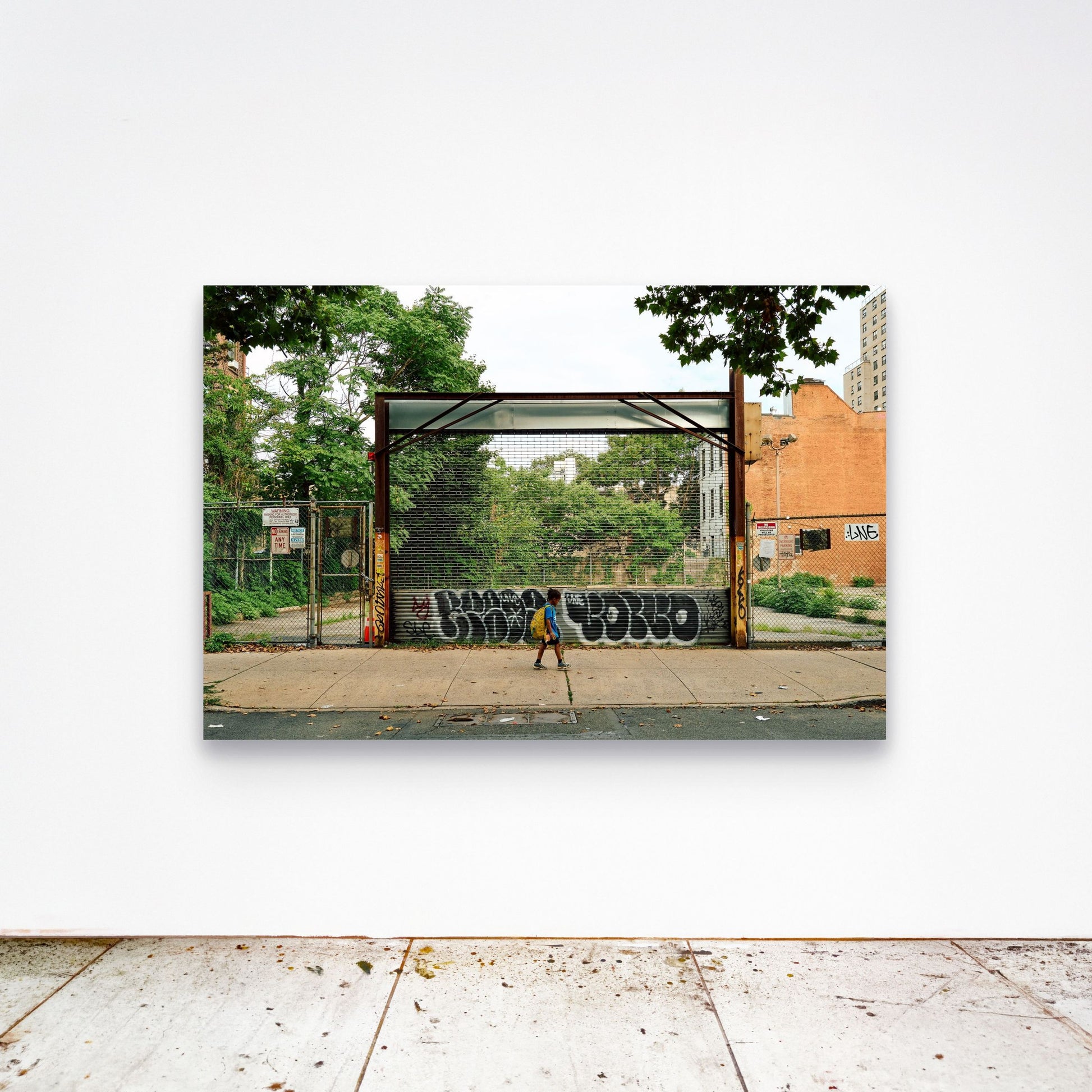 Chloe Albert's fine art print 'Boy Walking' shown unframed at 60 by 40 inches on a gallery wall above a concrete floor, displaying the large statement size in a room.